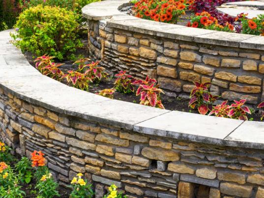 A residential retaining wall, up close and beautifully landscaped with colorful flower beds and bushes.