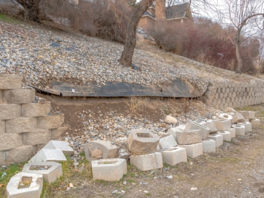 A close-up of a neighborhood retaining wall that is damaged and falling apart. The bricks are falling on the ground.