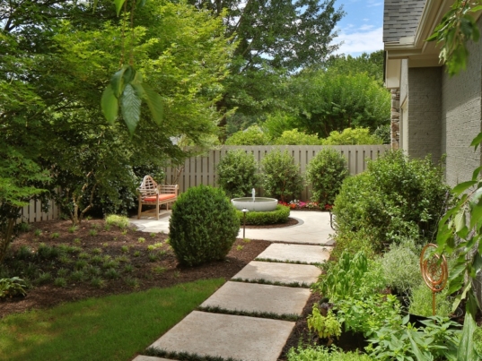 A beautifully landscaped backyard with customized hardscaping features, such as a water fountain and stepping pavements.