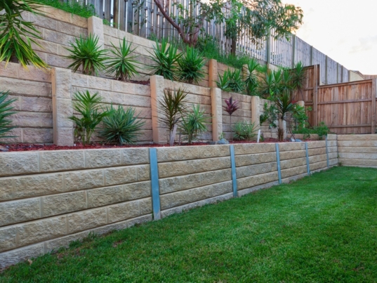 Three separate levels of retaining walls made out of tan-colored stone. Each level contains plants and rocks.