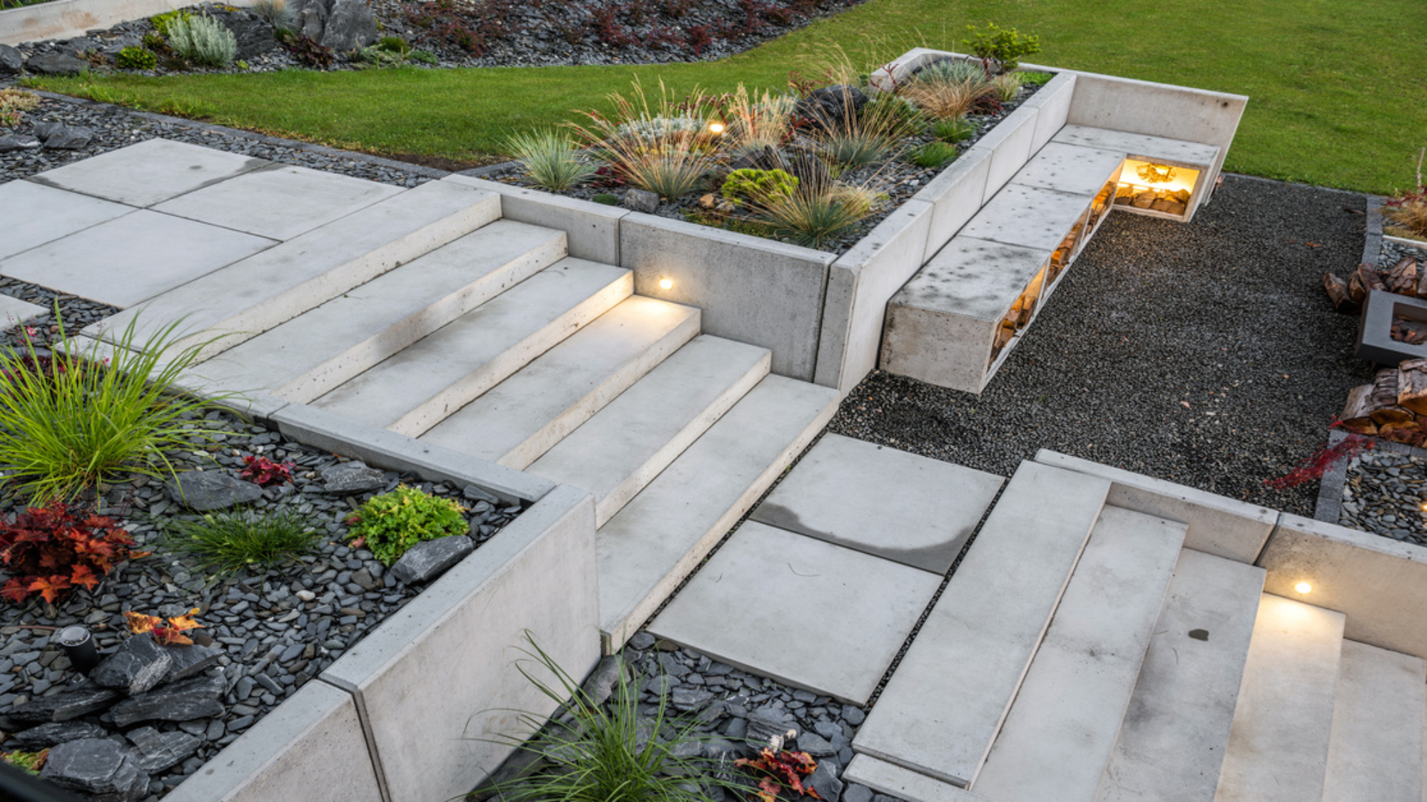 Light-gray colored concrete stairs and retaining walls surrounding landscape in a backyard by a grill.