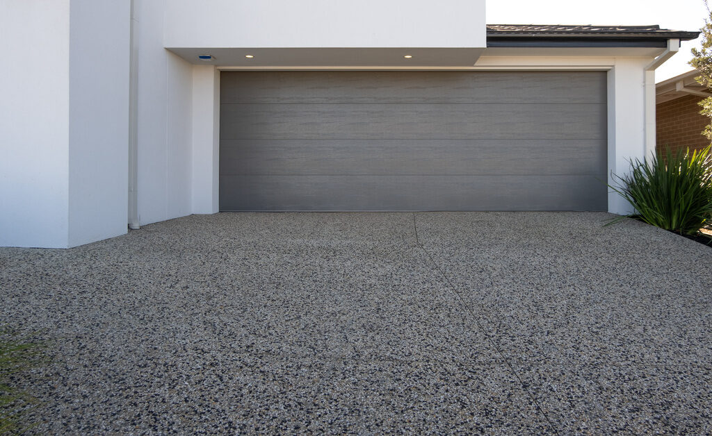 An exposed aggregate concrete surface used for a driveway at a white-colored modern residential home.