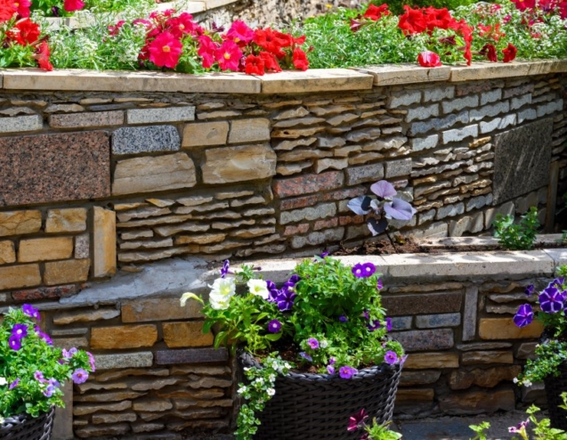 Multiple levels of stone retaining walls that enclose flowers beds filled with different colored flowers.