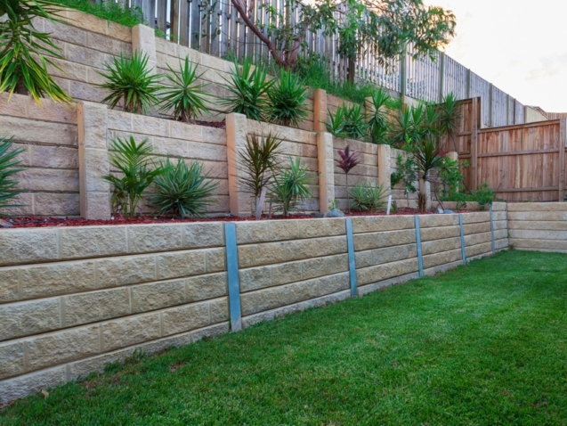A multi-level retaining wall constructed with light-colored stones. There are plants strategically placed in each tier.