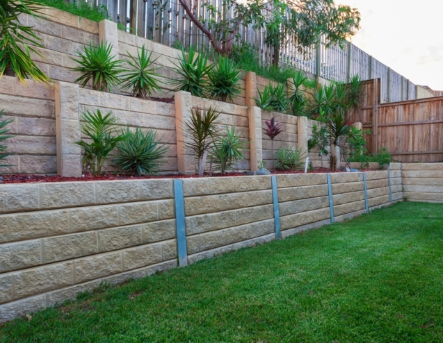 A multi-level retaining wall constructed with light-colored stones. There are plants strategically placed in each tier.