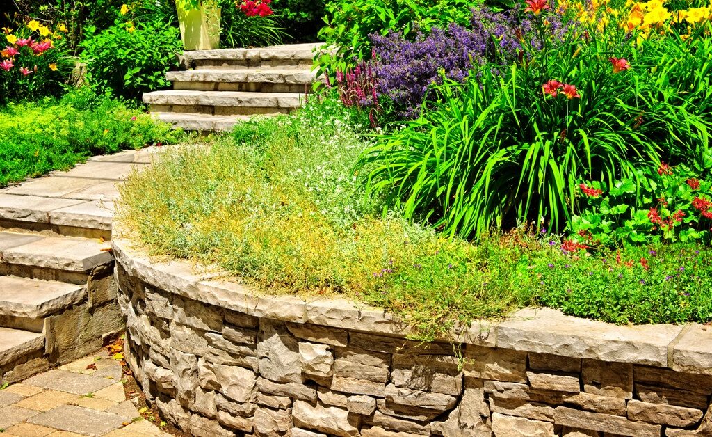 A natural light-colored stone retaining wall framing the landscaping that lines a staircase in a residential front yard.