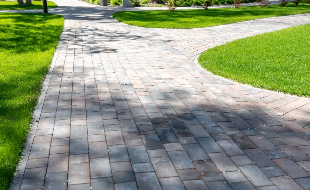 A curved paver walkway winds through a green lawn, creating a patterned path across the landscaped property.