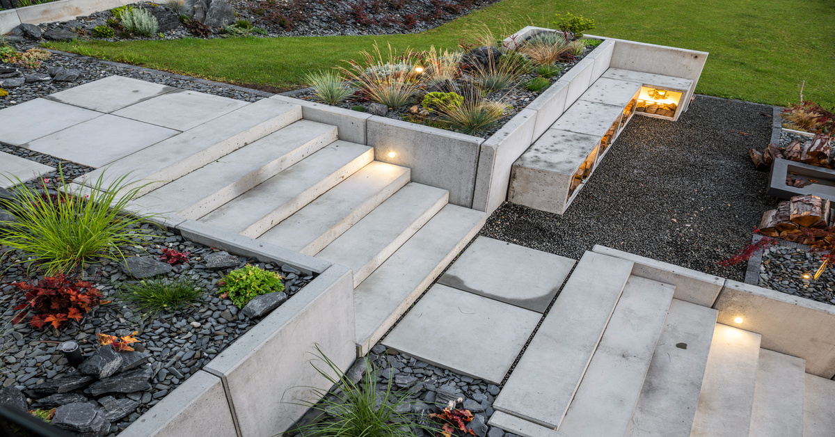 Light-gray colored concrete stairs and retaining walls surrounding landscape in a backyard by a grill.