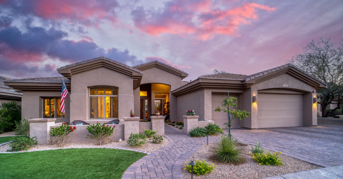 A large residential home with a stone walkway lined by rocks and grass patches containing small bushes.