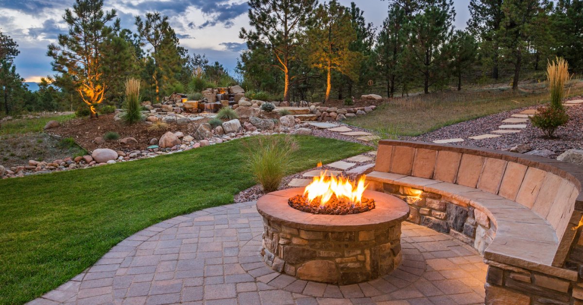 A stone retaining wall that also acts as part of a bench near the fire pit in the backyard of a home.